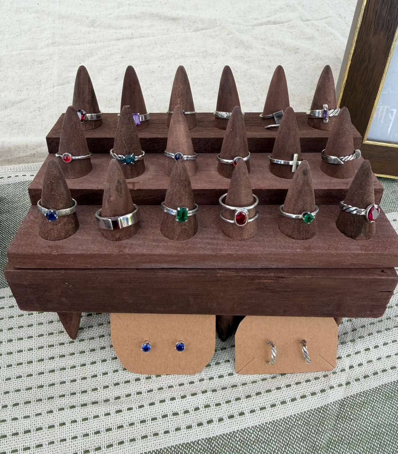 Sterling silver rings with lab-grown gemstones, gemstone studs, and twisted silver earrings on a wooden display stand